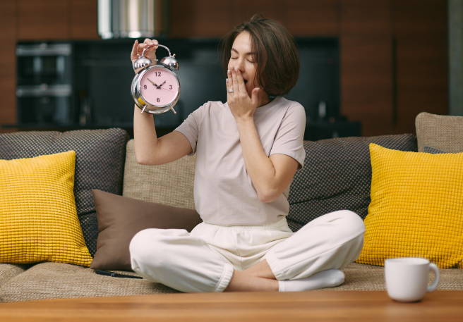 Frau hält Wecker und gähnt